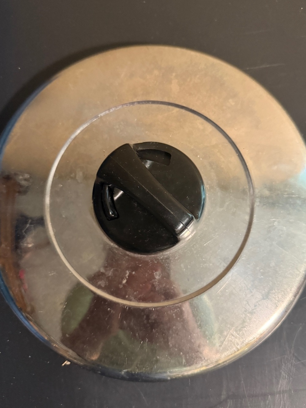 round, stainless steel cookware lid with a black central knob,